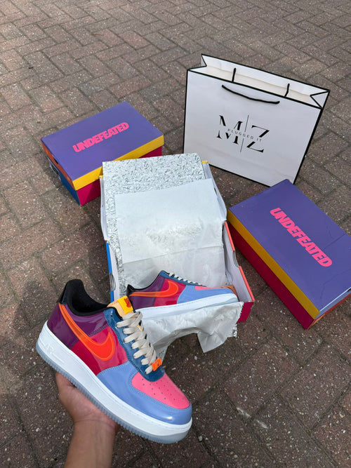 Colorful sneaker displayed with MZ and Undefeated branded boxes on a brick surface